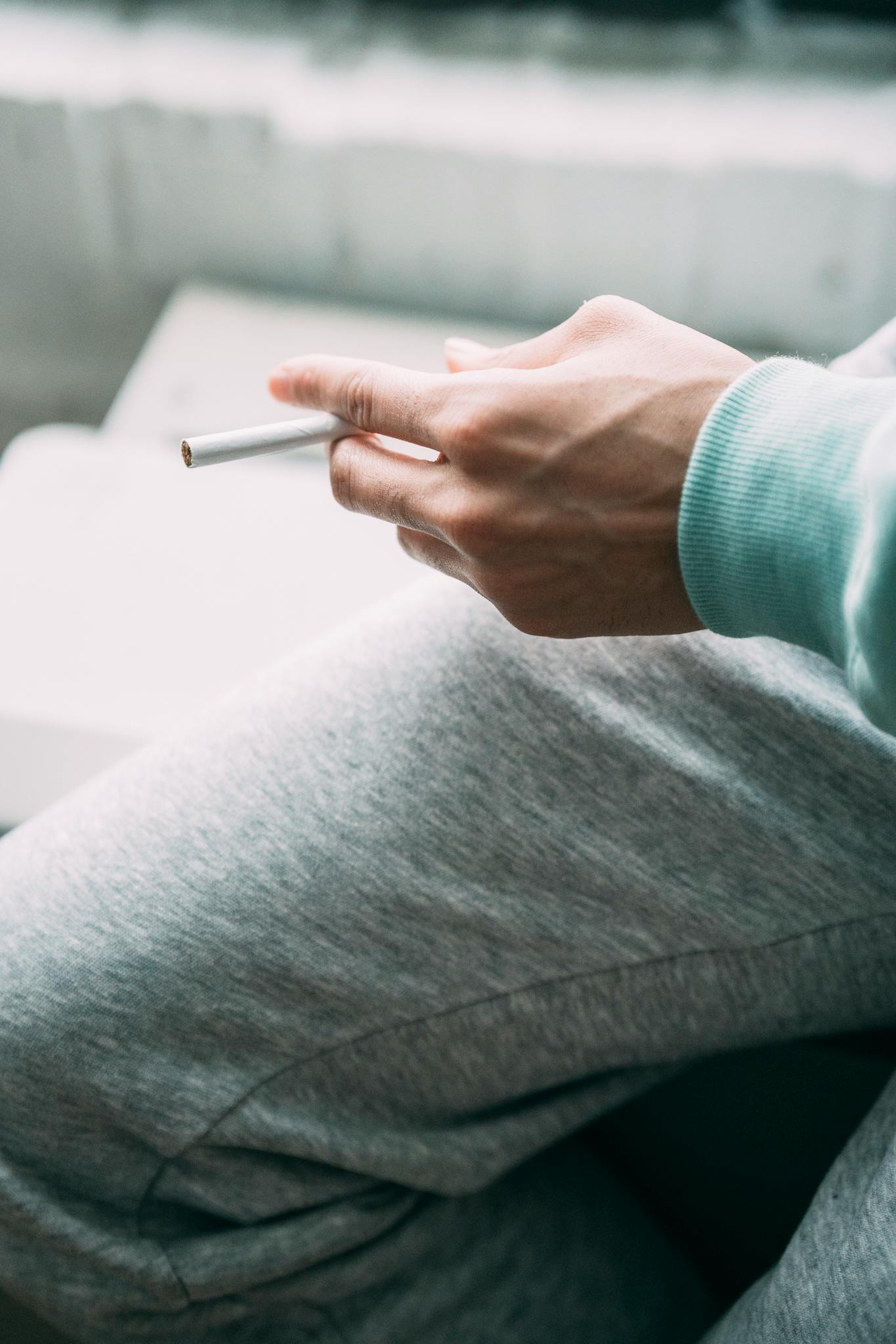 A person in casual sportswear sits indoors holding a cigarette, conveying leisure and calm.