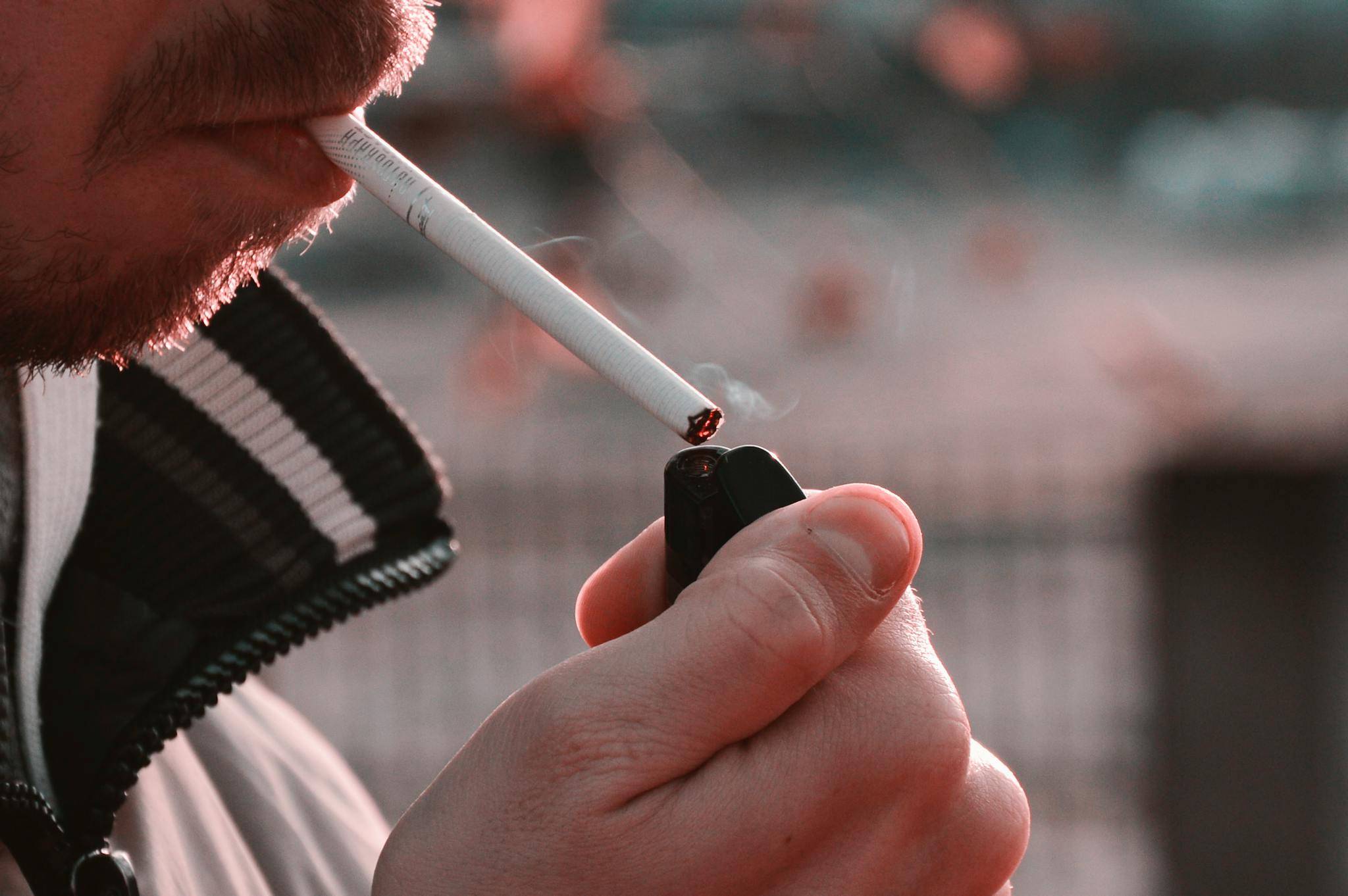 Close-up image of a person lighting a cigarette with a lighter outdoors, highlighting smoking habits.