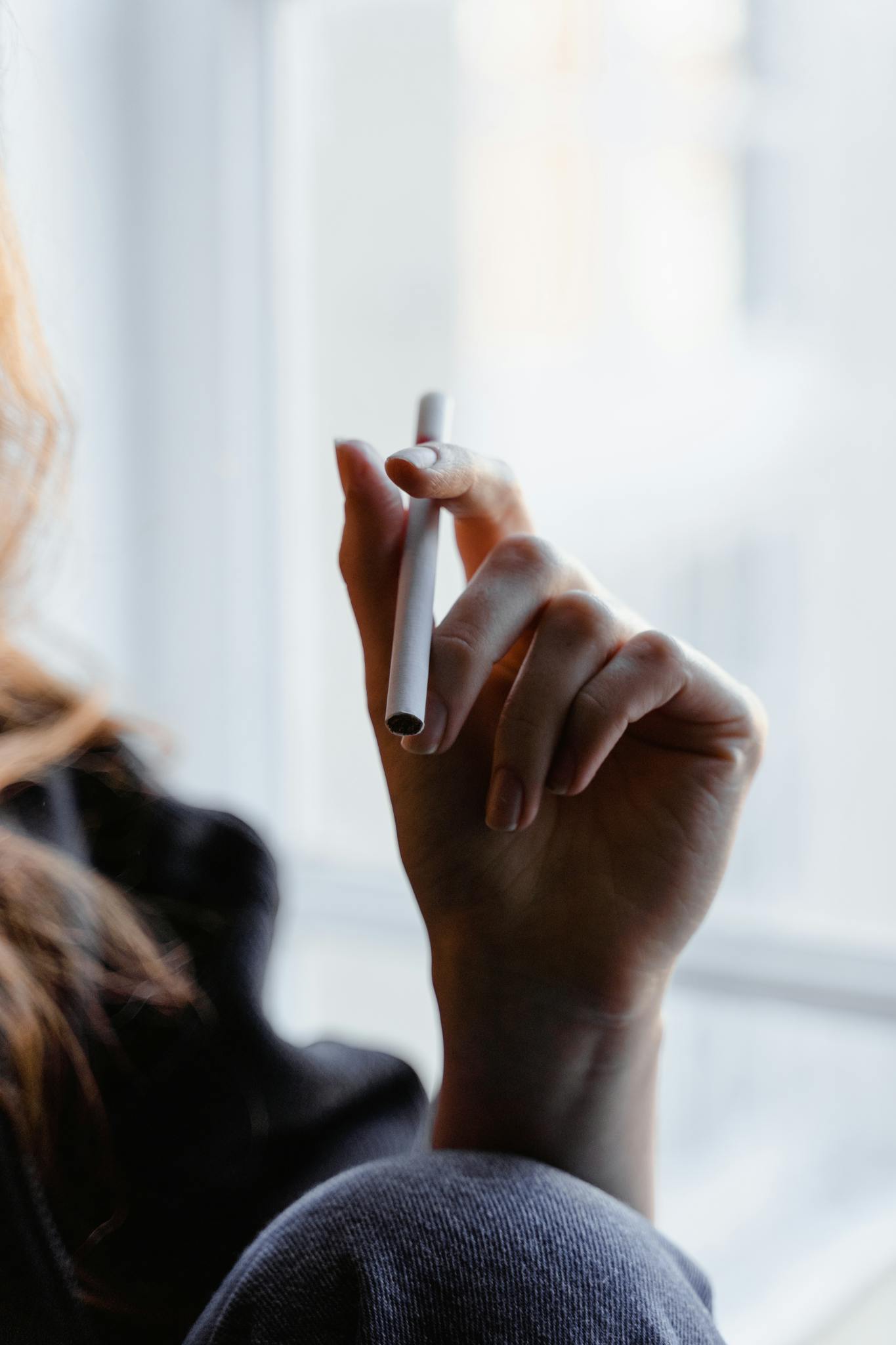 Close-up shot of a person holding an e-cigarette indoors, soft light.