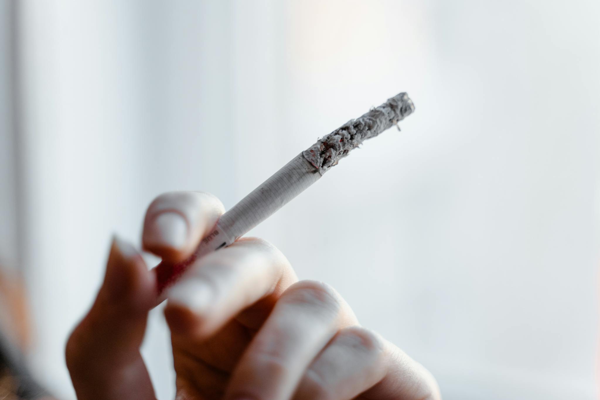 Detailed close-up of a hand holding a lit cigarette with ashes dropping.