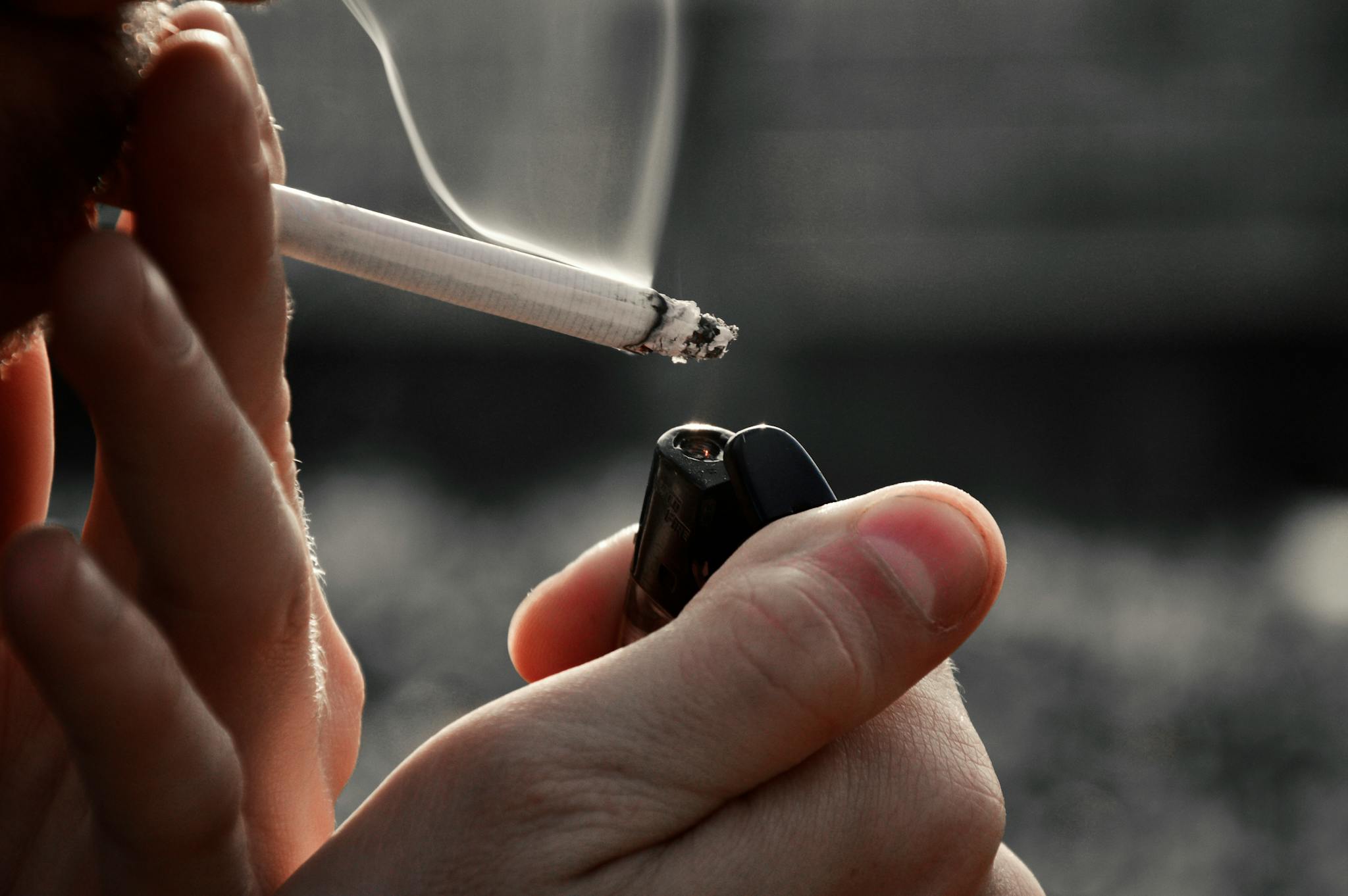 Detailed image of hands holding a cigarette and lighter, emphasizing smoking habit.